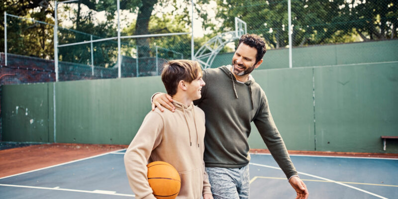 Father and son walking after playing a game of basketball. Young man and teenage boy having fun, talking and chatting while staying fit, active Father and son walking after playing a game of basketball. Young man and teenage boy having fun, talking and chatting while staying fit, active