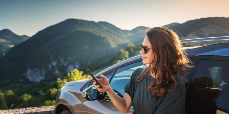 Young beautiful woman traveling by car in the mountains using smartphone at sunset, summer vacation and adventure Young beautiful woman traveling by car in the mountains using smartphone at sunset